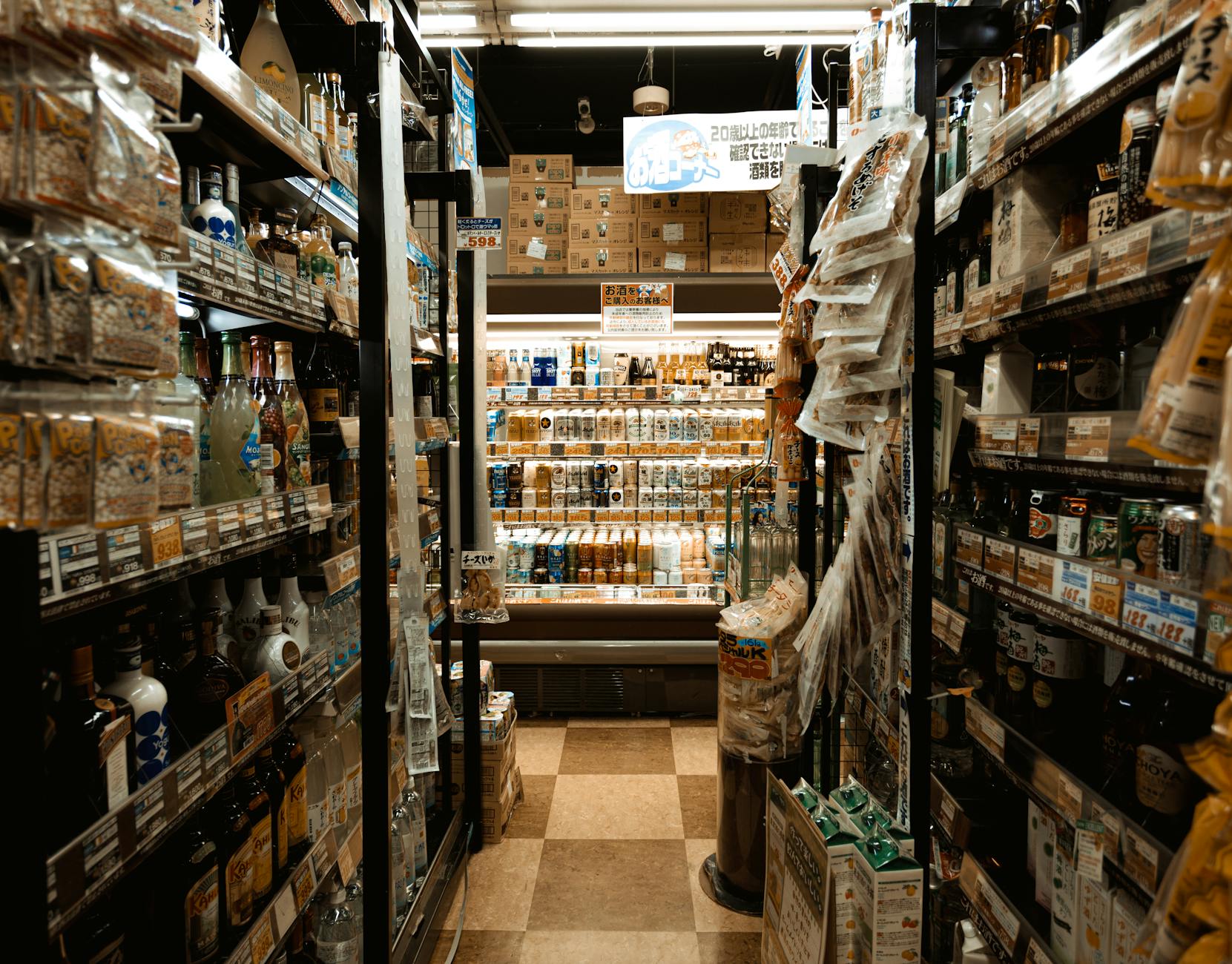 Empty convenience store aisle lit at night with shelves full of drinks and snacks